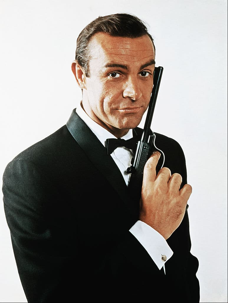 Retrato de cintura para arriba de Sean Connery, agarrando una pistola.
