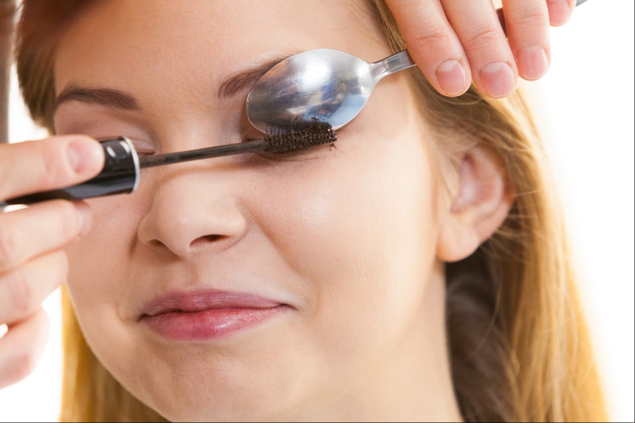 Woman trying new beauty viral trend. Woman applying mascara on eyelashes using small spoon.