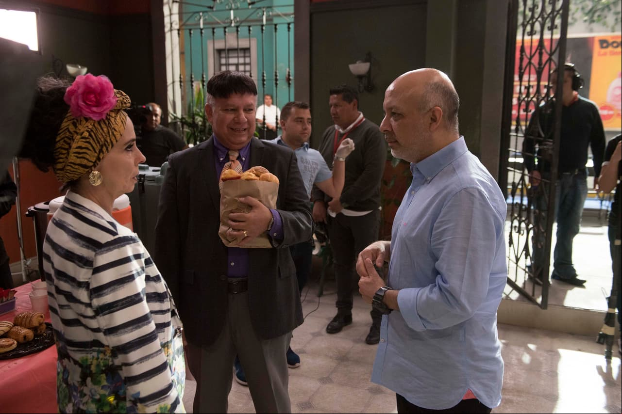 El productor dándole instrucciones a Doña Magda, mientras Arturo se roba el pan del catering.