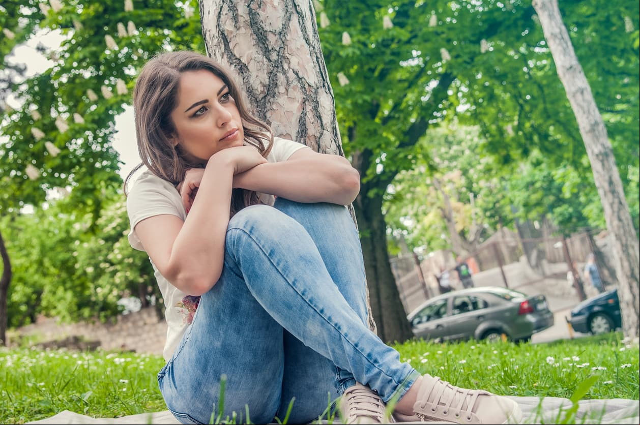 Close up of sad young woman deep in thought outdoors. Portrait of young cute elegant woman sitting outdoor. She is sad