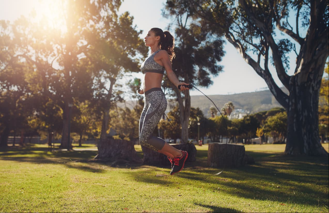 Full length portrait of fit young woman skipping with a jump rope in the park on a summer day.