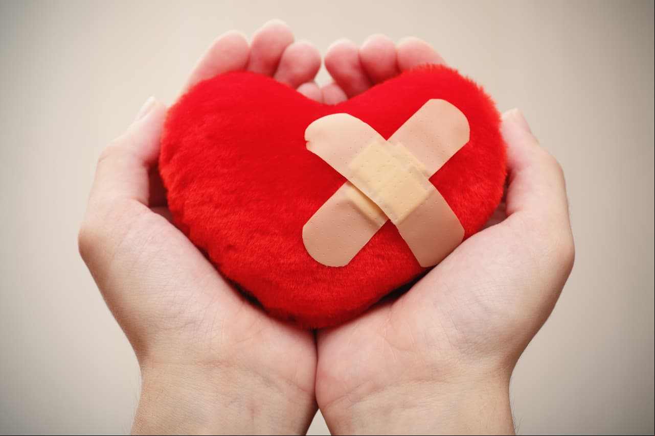 Red heart shape with cross bandaid in palms.